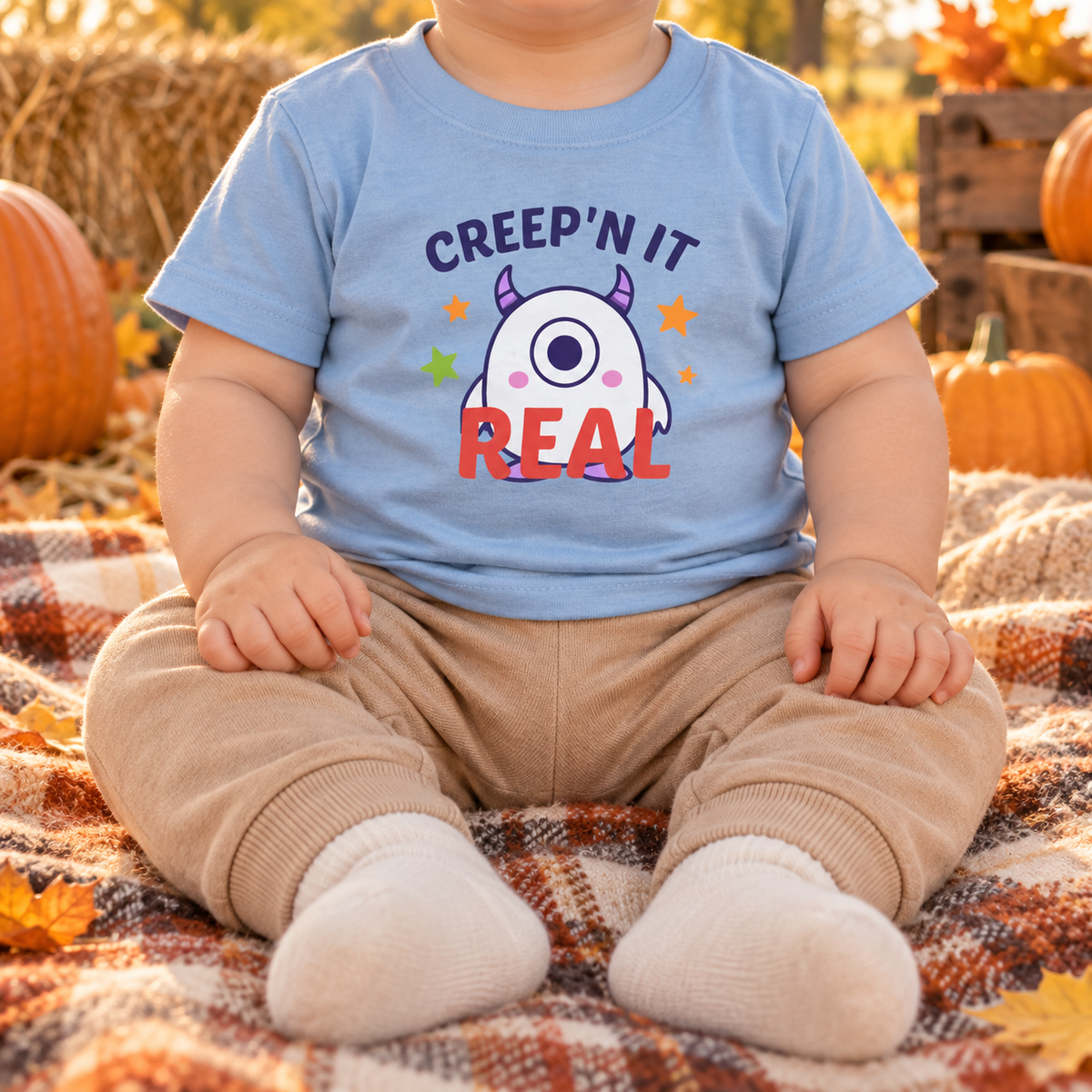 Infant wearing the updated light blue Creep'n It Real T-shirt at an autumn pumpkin picnic