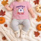 Overhead mockup of an infant wearing the updated pink Creep'n It Real T-shirt with autumn accents