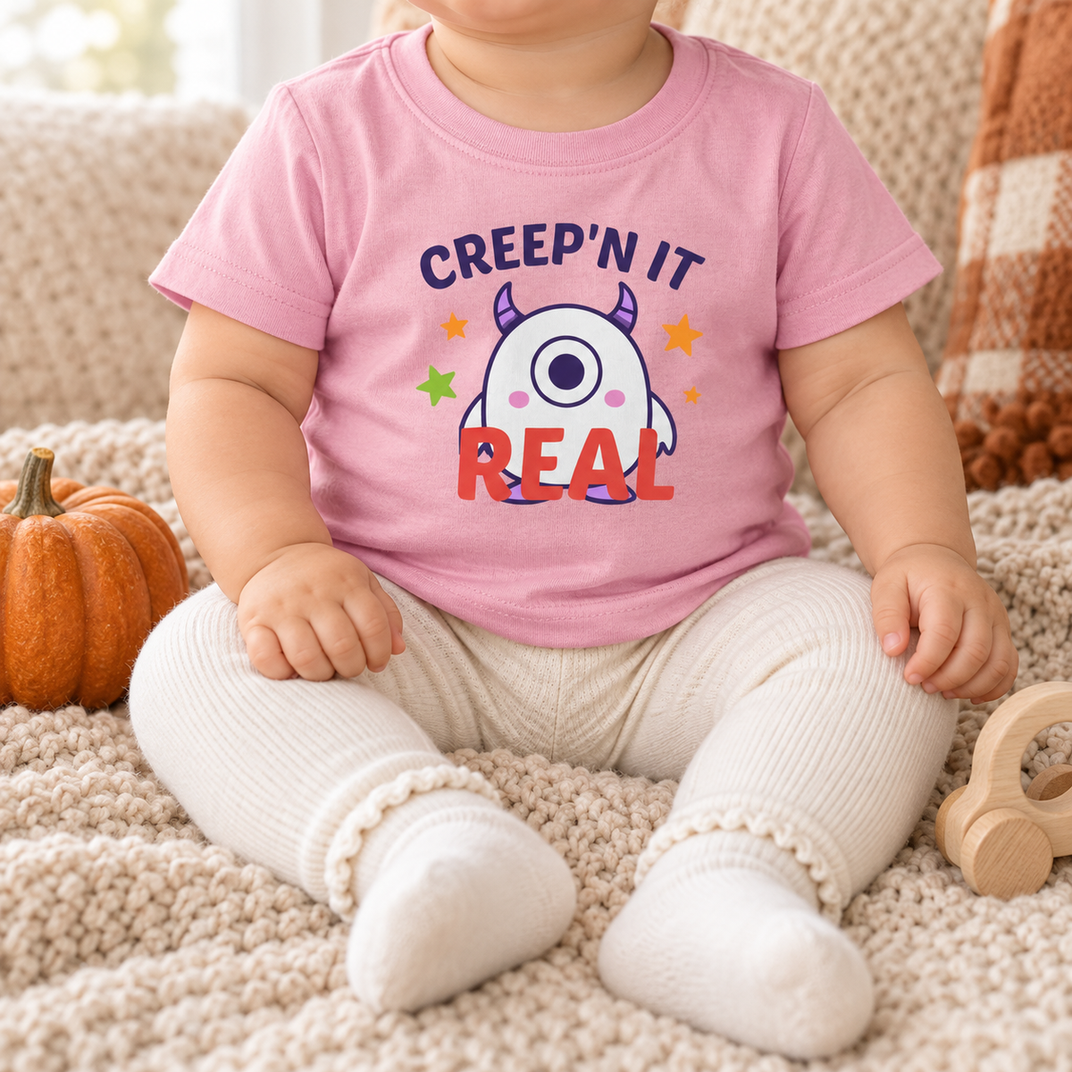 Infant wearing the updated pink Creep'n It Real T-shirt on a cozy fall blanket